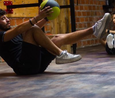 A man and woman perform core exercises with a medicine ball in a brick wall gym.